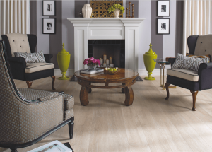 A stylish living room with two armchairs, a wooden coffee table with flowers, a white fireplace with candles, decorative yellow vases, framed wall art, and light wood floors.