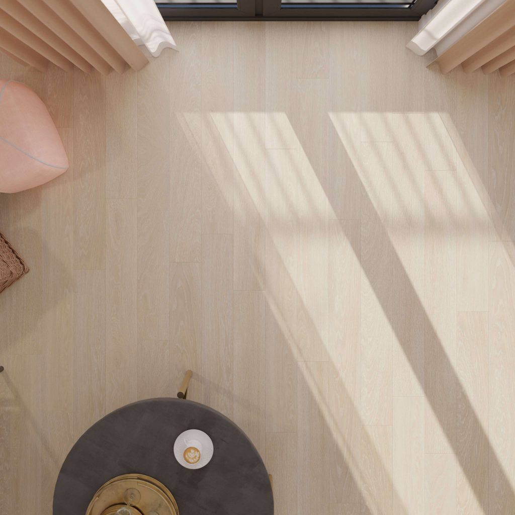 A top view of Estate Oak Beige flooring with sunlight and shadows, showing the edge of a round black table with a gold-handled teacup, a woven basket, and a pink chair in the corners.