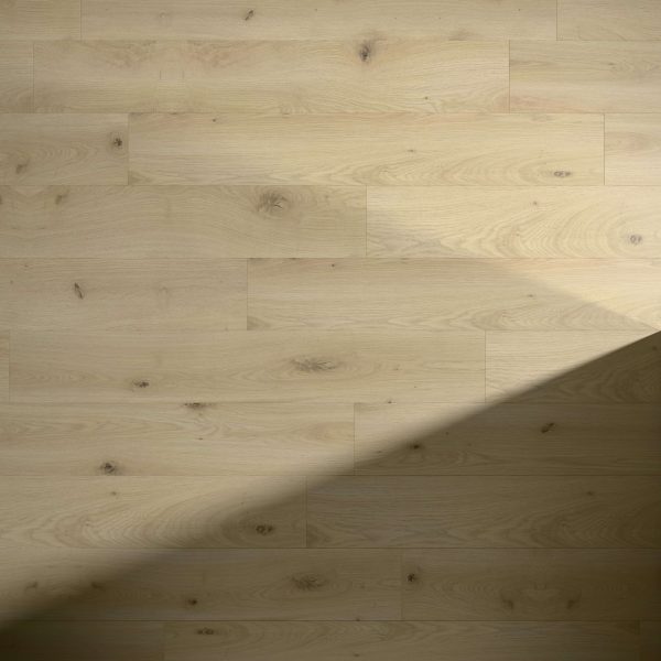 Kortemark Oak features light-colored wooden floorboards with distinct natural grain and knots. A shadow falls diagonally across the lower right corner, highlighting the contrast between illuminated and shaded areas.