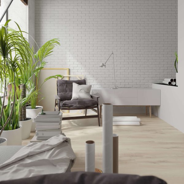 A modern, minimal living space featuring Charleroi Oak flooring, potted plants, a gray armchair with cushions, stacked books, rolls of paper, and a white brick wall for a cozy, creative vibe.