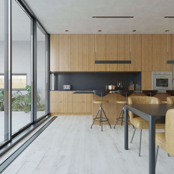 The Inland* kitchen features wood cabinets, black countertops, high black stools, a tan-chair dining table, and expansive floor-to-ceiling windows with views of lush greenery.
