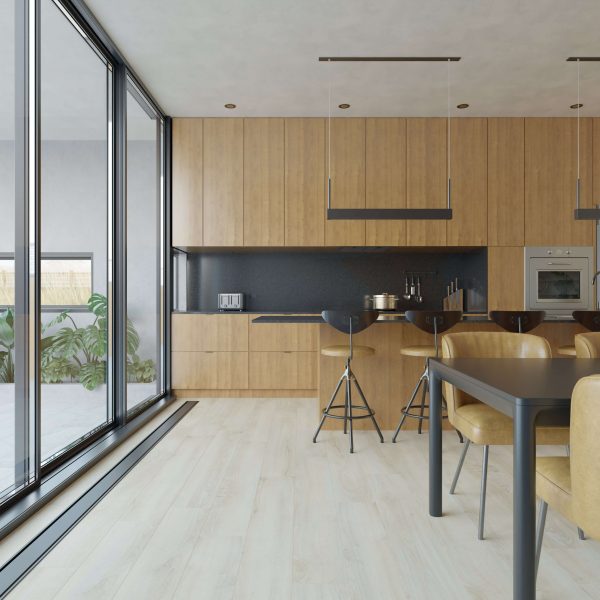 The Sandilands* kitchen features light wood cabinets, a black backsplash, built-in appliances, and bar stools at the counter. Large glass doors provide natural light, with views of green plants and a dining area with tan chairs.