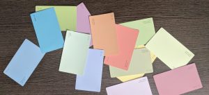 A scattered arrangement of pastel-colored paint sample cards lies on a dark wooden surface, featuring shades like blue, green, yellow, pink, and peach.
