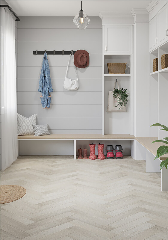 Bright mudroom with white walls, a bench, cubbies, and hooks holding a hat, bag, and denim shirt. Pink rain boots and shoes are under the bench. A window and hanging light provide natural and soft lighting.
