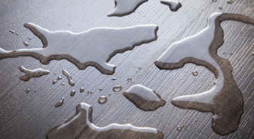 Water spilled on a dark wooden surface, forming irregular shapes and reflecting light.